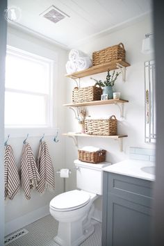 a white toilet sitting in a bathroom next to a sink and shelves filled with towels