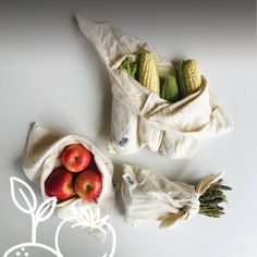 two bags filled with fruit sitting on top of a white table next to an ear of corn