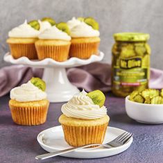 cupcakes with white frosting and pickles are on a plate next to a jar of pickles