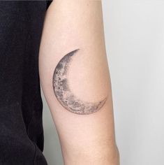 a small crescent moon tattoo on the left upper half of the arm is black and white