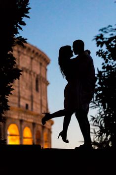 the silhouette of a couple kissing in front of an ancient building at dusk, with their arms around each other