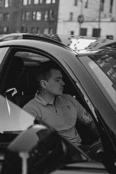 a man sitting in the driver's seat of a car with tattoos on his arm