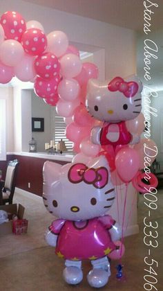 a hello kitty balloon with pink and white balloons attached to it, sitting on top of a table