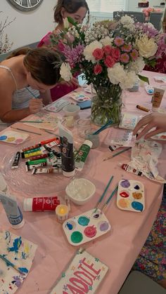 two women are painting on a table with flowers in the vase and other art supplies