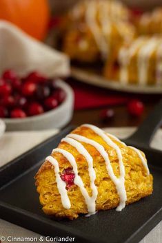 a piece of cake with icing sitting on top of a black plate next to some cranberries