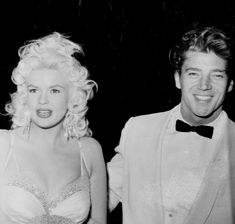 a man in a tuxedo standing next to a blonde haired woman wearing a bra