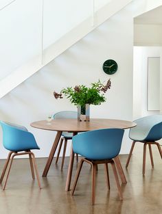 a wooden table with blue chairs under a stair case next to a clock and plant