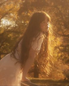 a woman with long hair sitting on top of a wooden bench in the sun light