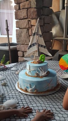 there is a blue cake with a sailboat on the top and sea shells around it