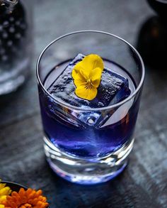 a glass filled with blue liquid and a yellow flower