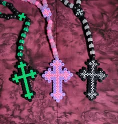 three beaded cross necklaces are laying on a pink fabric sheet with black and white beads