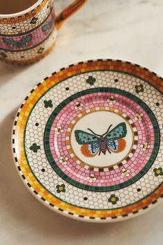 a plate with a butterfly painted on it next to a cup filled with tea and coffee