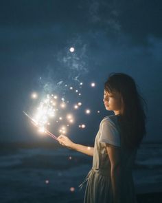 a woman holding sparklers in her hand on the beach