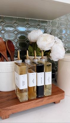 three bottles of liquid sitting on top of a wooden shelf next to a white flower