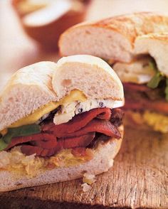 two sandwiches with meat, cheese and lettuce are on a wooden cutting board