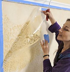 a woman is painting a wall with white laces on it and she is holding a paint roller in her right hand