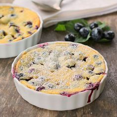 two blueberry pies sitting on top of a wooden table next to each other