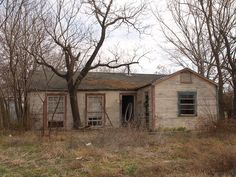 an old run down house sitting in the middle of a field next to some trees