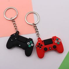 two video game controllers key chains on a pink and green background with a black one