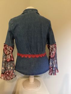 the back of a denim jacket with red and blue flowers on it, sitting on top of a mannequin