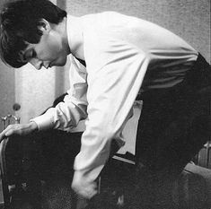 a black and white photo of a man bending over to look at something on the floor