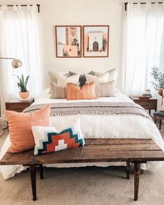 a bed with pillows on top of it next to two pictures and a bench in front of the bed