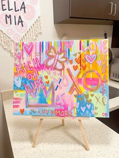 a colorful painting is on an easel in a kitchen with the name ella mia above it