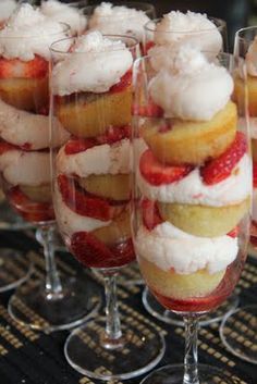 several desserts are arranged in wine glasses on a table with strawberries and whipped cream