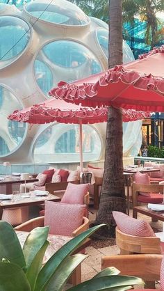 an outdoor dining area with pink chairs and umbrellas in front of large circular windows