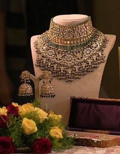 an elaborate necklace and earrings on display in a room with roses, vases and other items