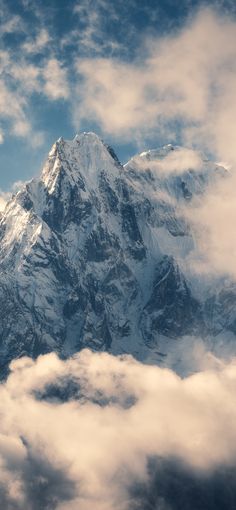 the top of a snow covered mountain with clouds below