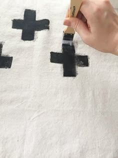 someone using a brush to paint the cross on a rug with black and white paint