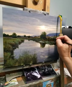 a person holding a paintbrush in front of an easel with a painting on it