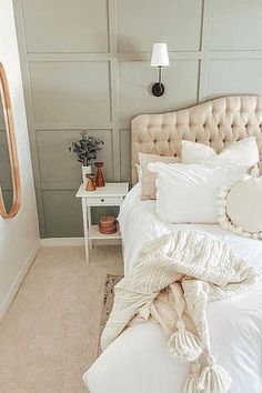 a white bed sitting in a bedroom next to a mirror and table with a lamp on it