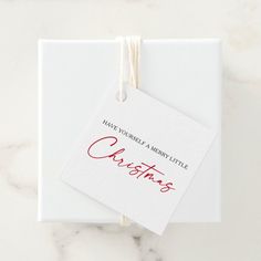 a white box with a red christmas tag hanging from it's side on a marble surface