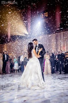 a bride and groom are kissing in front of confetti falling from the ceiling