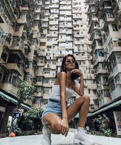 a woman sitting on the ground in front of tall buildings