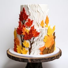 a multi - layered cake decorated with fall leaves on a wooden stand against a white background