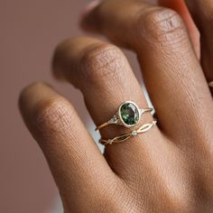 a woman's hand wearing a gold ring with a green tourmaline stone