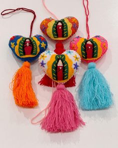 four colorful heart shaped ornaments with tassels hanging from the top, on a white surface