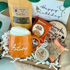 an orange coffee mug filled with goodies in a gift box on top of a blanket