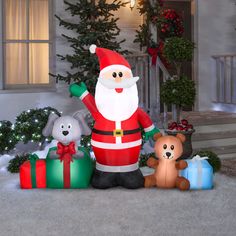 an inflatable santa clause standing next to two teddy bears and a christmas tree