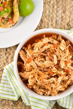 a white bowl filled with shredded chicken next to a lime