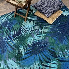 a blue and green area rug with palm leaves on it, next to a small wooden table