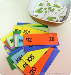 a bowl filled with lots of different colored numbers next to a pile of numbered cards