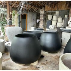 several large black vases sitting on top of cement pots in a room with brick walls