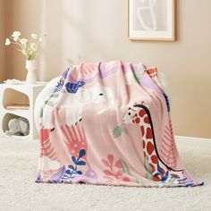 a pink blanket with giraffes and leaves on it sitting on the floor