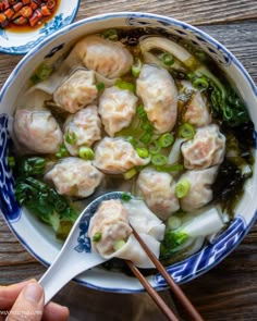 a blue and white bowl filled with dumplings and greens next to a wooden table