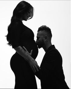 a pregnant woman standing next to a man with his hand on the belly of her stomach