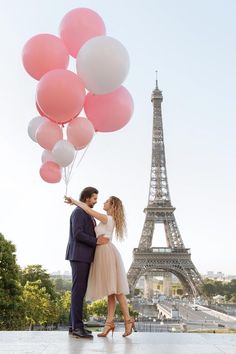 a man and woman standing in front of the eiffel tower with pink and white balloons